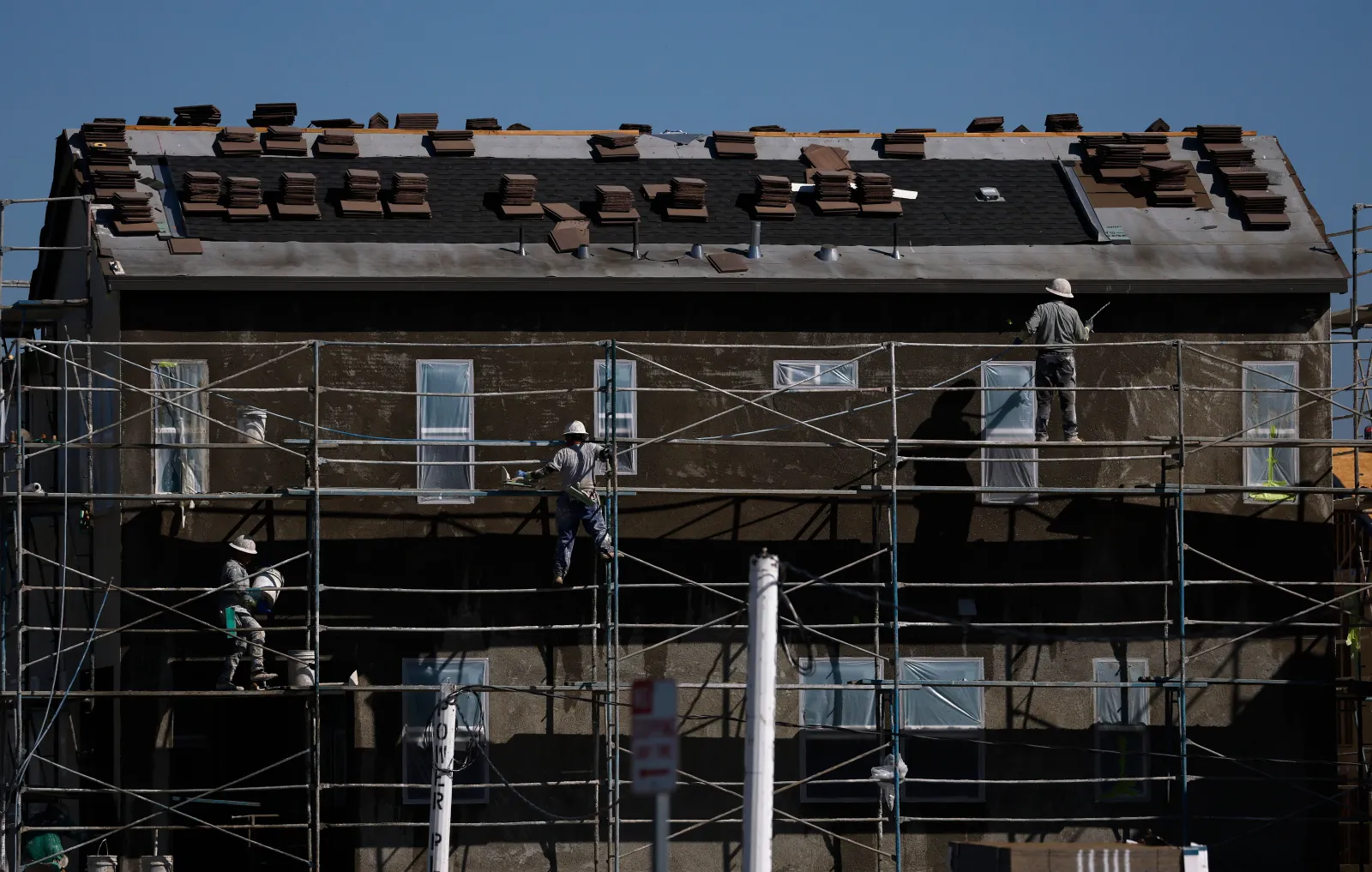 workers stand on scaffolding at a home under construction at a development, Valencia, California, June 24, 2026.