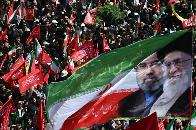 Mourners wave a flag bearing the portraits of Iran's current supreme leader Mojtaba Khamenei (L) and his his slain father Ali Khamenei during a funeral procession for Iran's slain supreme leader Ali Khamenei and members of his family in Tehran on July 6, 2026.