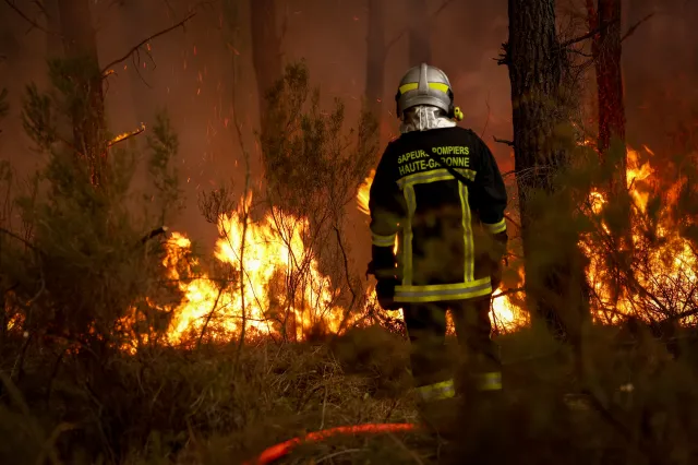 A firefighter stands before flames as a forest fire rages in Saint-Jean-d'Illac, 20 miles from Bordeaux, on July 26, 2026 as a wildfire has been ravaging the forest north of the Arcachon Basin (Gironde).