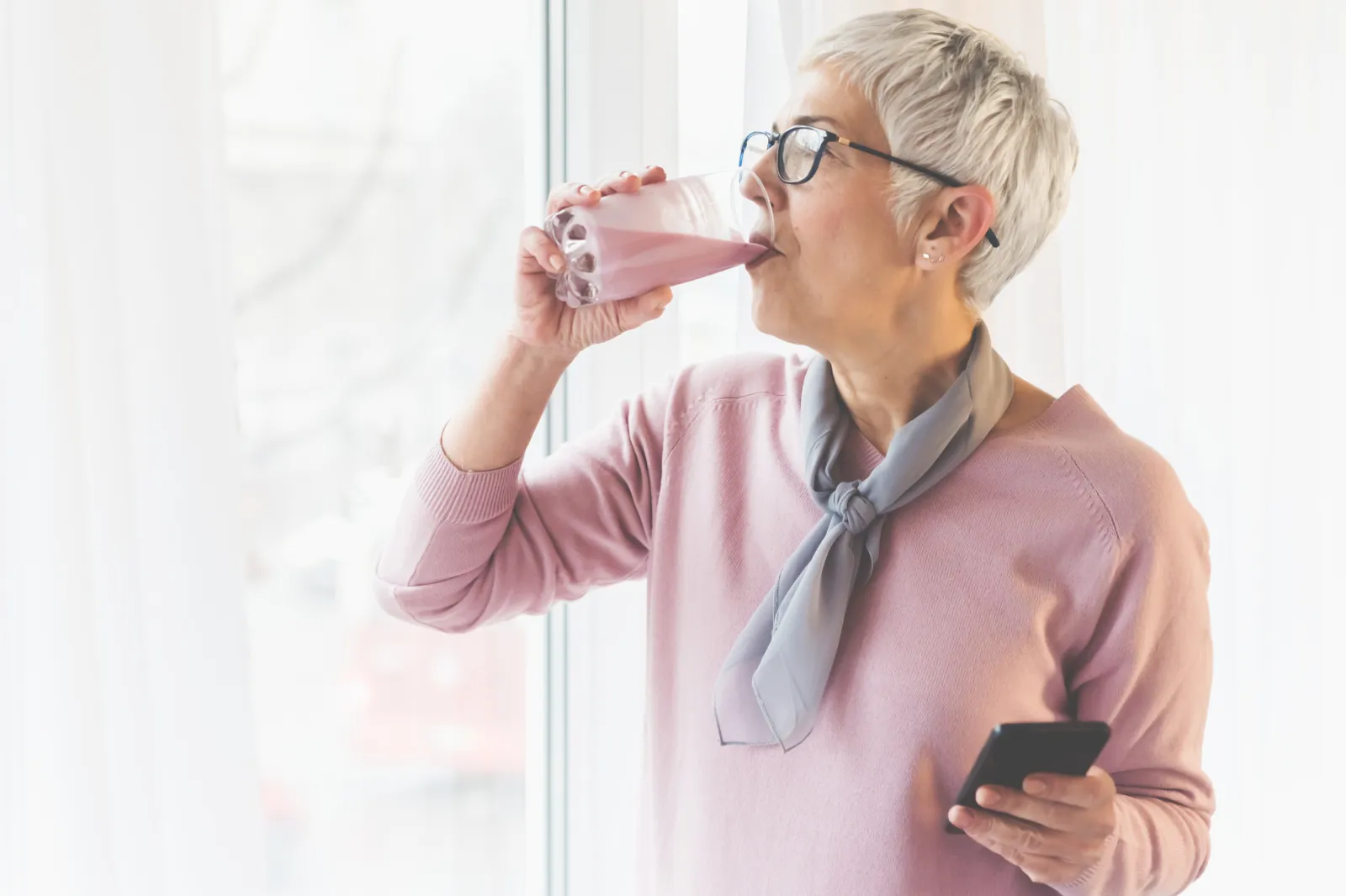 A stock photo of a senior woman drinking by the window.