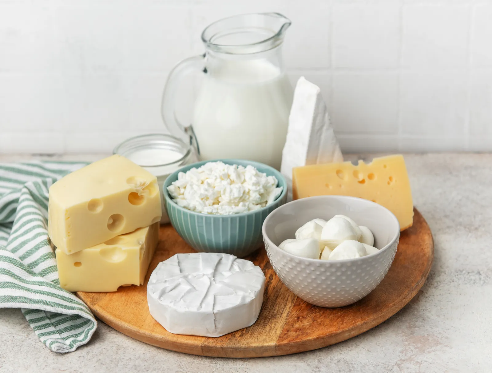  various cheeses and milk are displayed on a wooden platter.