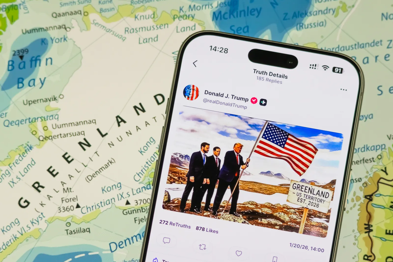 In this photo illustration, a smartphone displays a post by U.S. President Donald Trump on the Truth Social platform showing a composite image featuring Trump alongside U.S. Secretary of State Marco Rubio and U.S. Vice President J.D. Vance, with the U.S. flag and a sign reading Greenland, U.S. Territory Est. 2026, against a map of Greenland.
