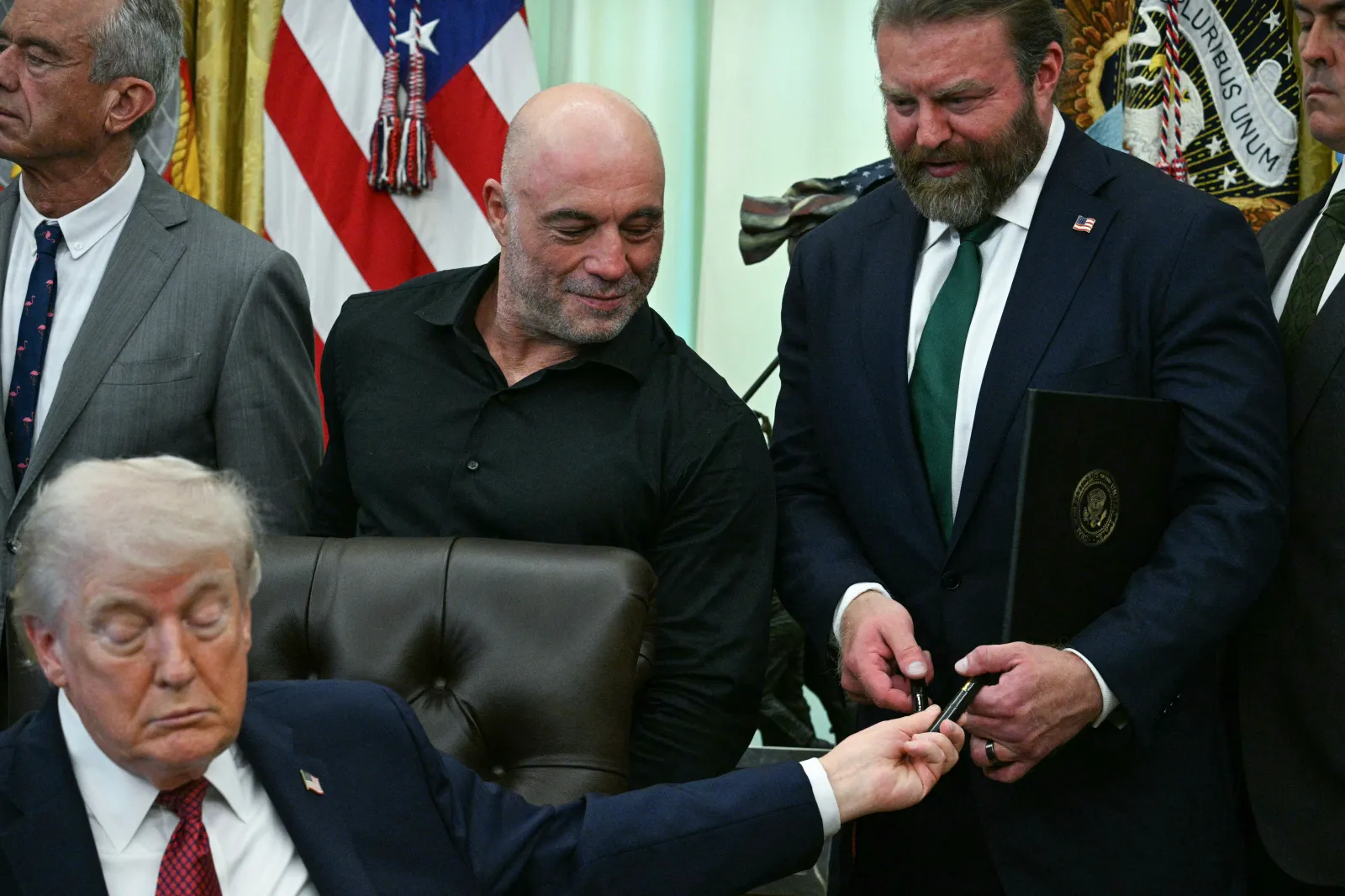 US media personality Joe Rogan (center L) looks on as US President Donald Trump hands out a pen at the White House on April 18, 2026. (Photo by Jim WATSON / AFP via Getty Images)