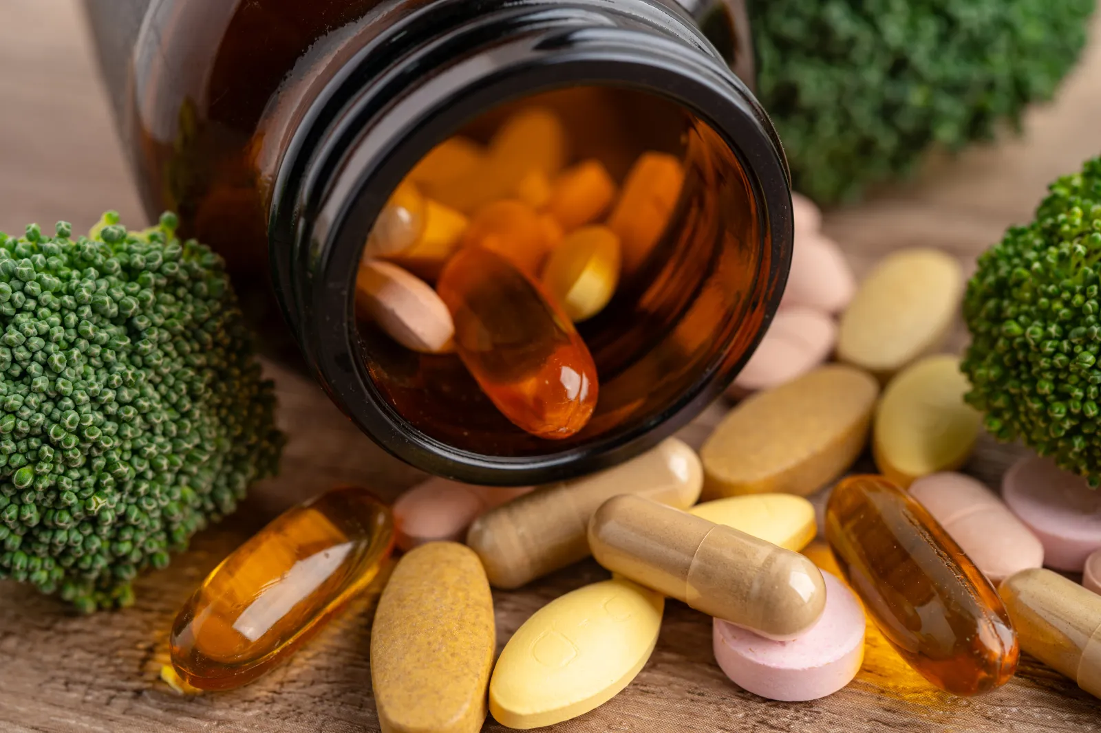 Stock image of vitamins spilling out of a bottle amid pieces of broccoli.
