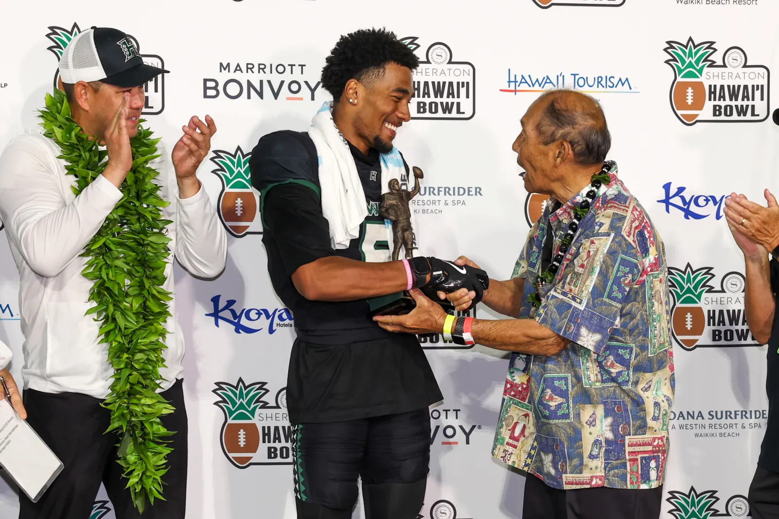 Pofele Ashlock #5 of the Hawai'i Rainbow Warriors (C) receives the Hugh Yoshida Most Valuable Player Award from Hugh Yoshida (R) as Head coach Timmy Chang looks on after the Sheraton Hawai'i Bowl at the Clarence T.C. Ching Athletics Complex on December 24, 2025 in Honolulu, Hawai'i.