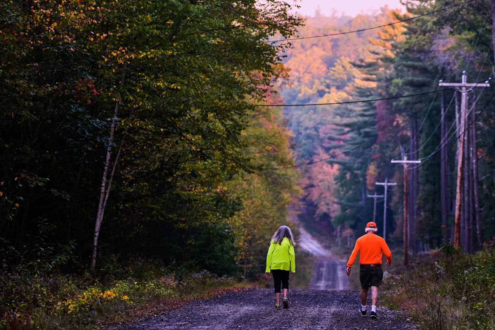 A couple, wearing protective high-visibility clothing due to hunting season, take a walk at dawn, as trees of in the distance turn to fall foliage colors, Tuesd