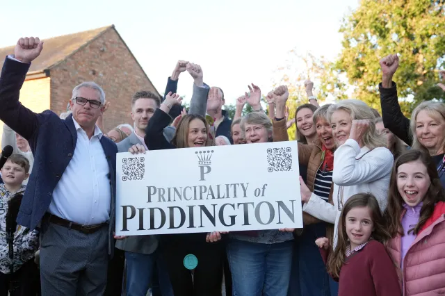 Local residents pose with a "Principality of Piddington" sign in the village of Piddington, Oxfordshire, England, Wednesday, Sept. 16, 2026, after they voted overwhelmingly to become an independent state in a symbolic "referendum".
