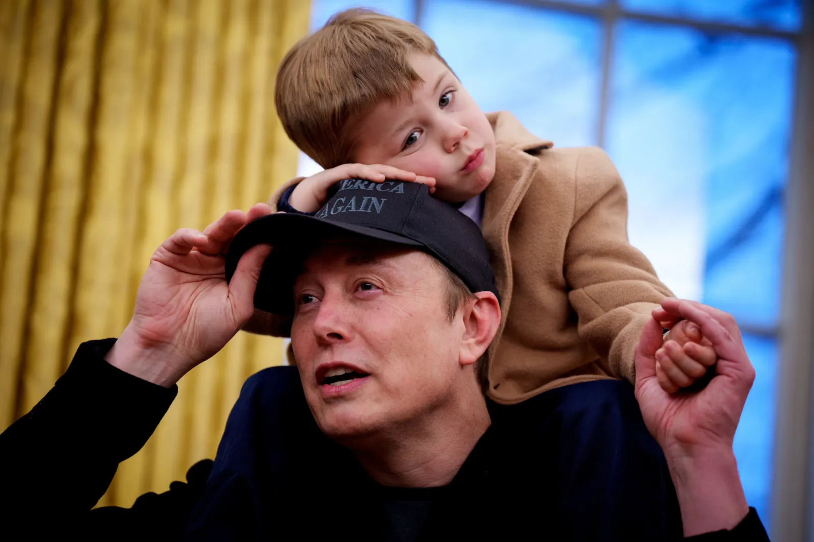 X Musk, whose mother is Grimes, sits on the shoulders of his father, Elon Musk, as he speaks to reporters during an executive order signing in the Oval Office a