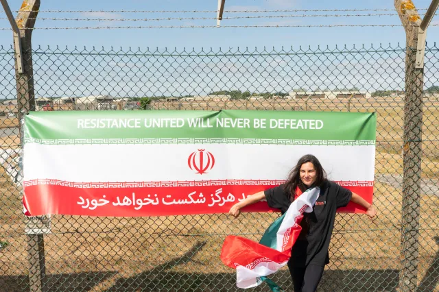 A woman stands by a banner with the Iranian flag and an anti-war message at RAF Fairford on August 15 in Fairford, England.