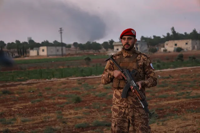 A Syrian military police officer stands guard as smoke rises in the distance following explosions at an army weapons depot in the Al-Hadaba area near Aleppo, Syria, on September 21, 2026.