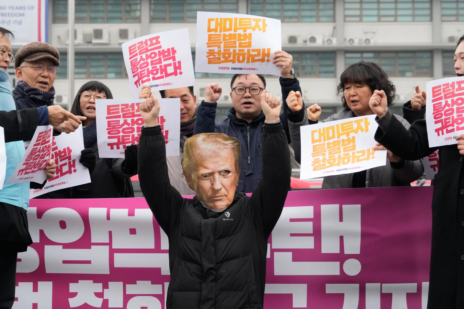 A South Korean protester, wearing a mask of U.S. President Donald Trump, gestures during a rally against Trump's tariff policy for South Korea, near the U.S. embassy in Seoul on February 11. The banners in red say "We condemn Trump's trade pressure." (AP Photo/Ahn Young-joon)