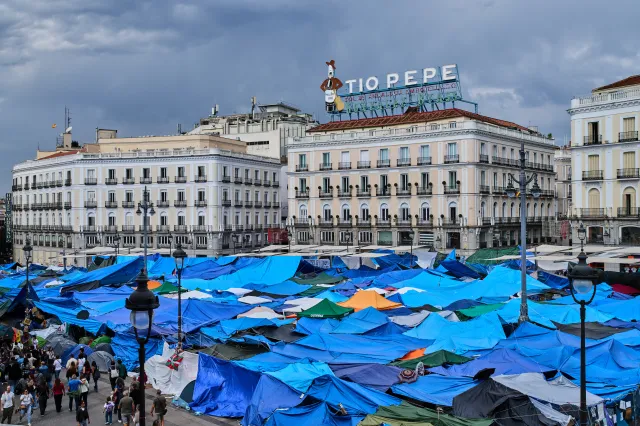 People walk among tents set up by protesters at the Puerta del Sol square demanding stronger laws to protect renters in Madrid on October 17.