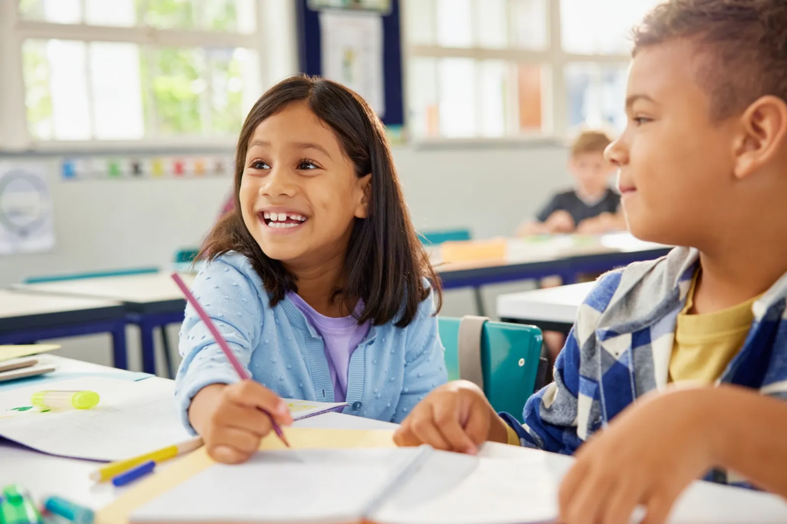 A happy smiling schoolgirl is helping her classmate in the classroom.