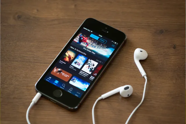 Stock image: an Apple iPhone with iTunes store application on the screen lies on a desk with earphones in 2014.