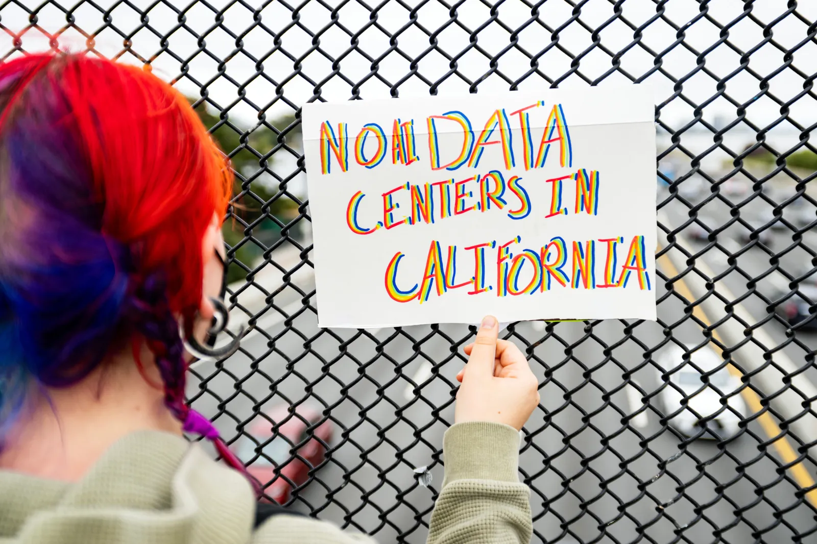 A person holds up a sign on a pedestrian bridge during a nationwide protest against AI data center expansion in Berkeley, California on July 18, 2026.