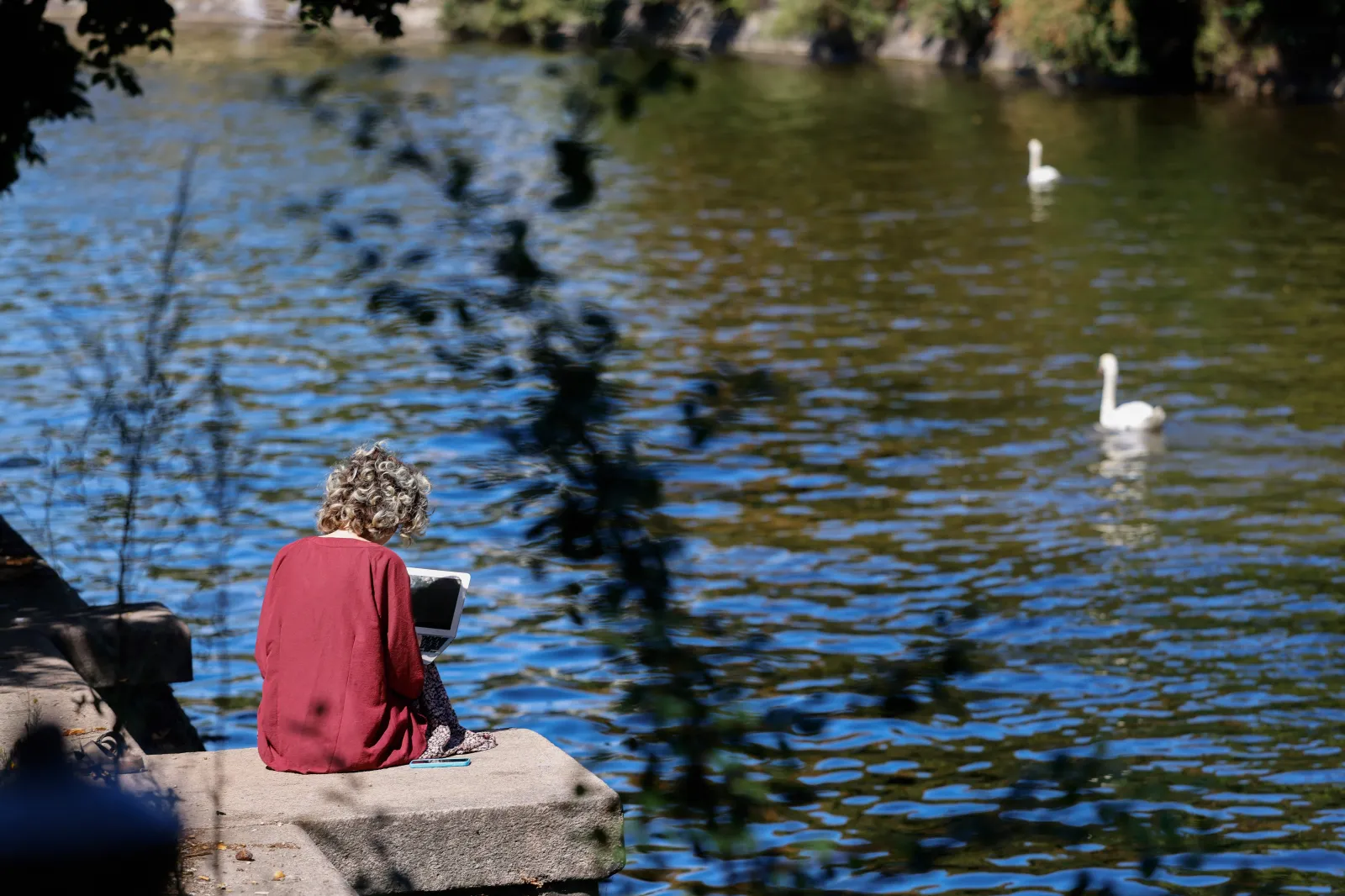 A woman uses a laptop as she sits on the banks of the Landwehr canal in Berlin's Neukoelln district as the sun shines on July 24, 2022.