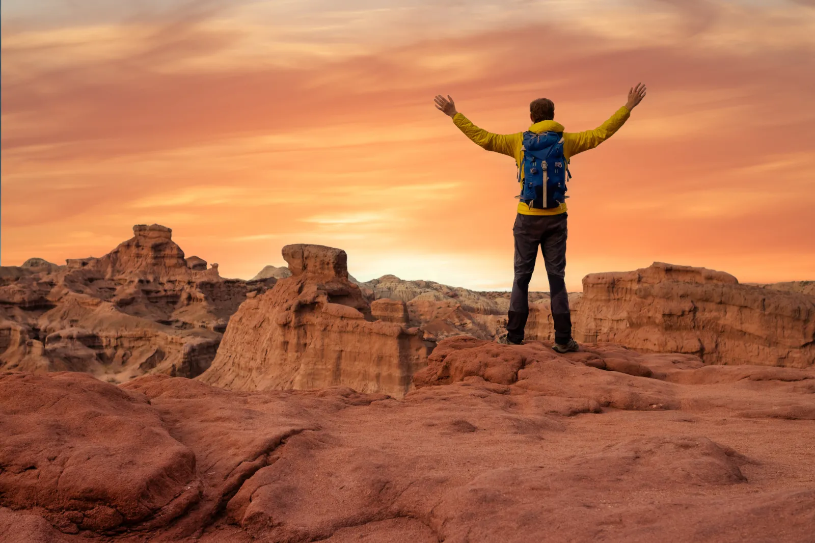 A man with his arms raised in the air at the top of a mountain peak.