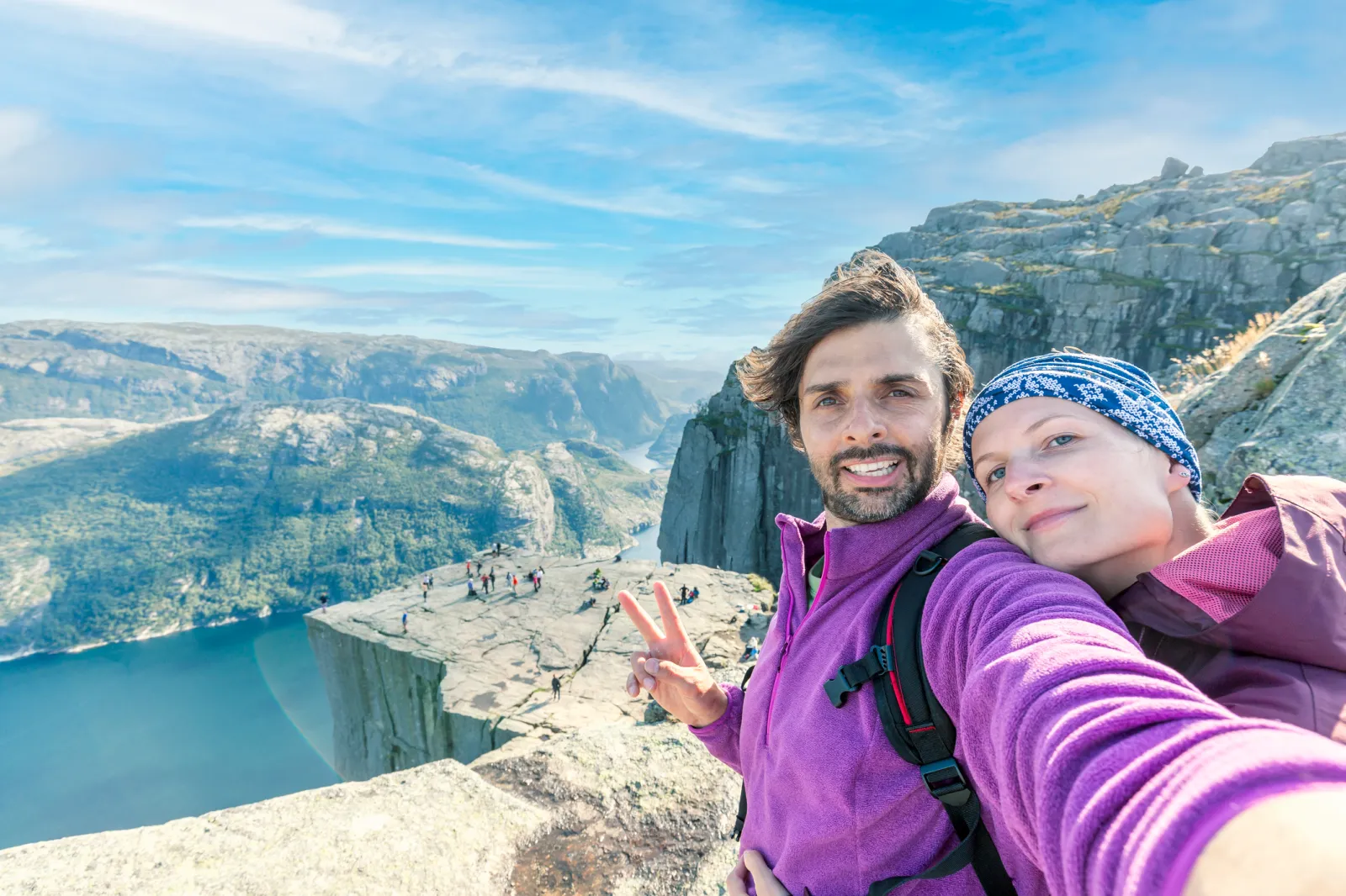 A couple posing for a selfie from a rock edge overlooking a fjord.