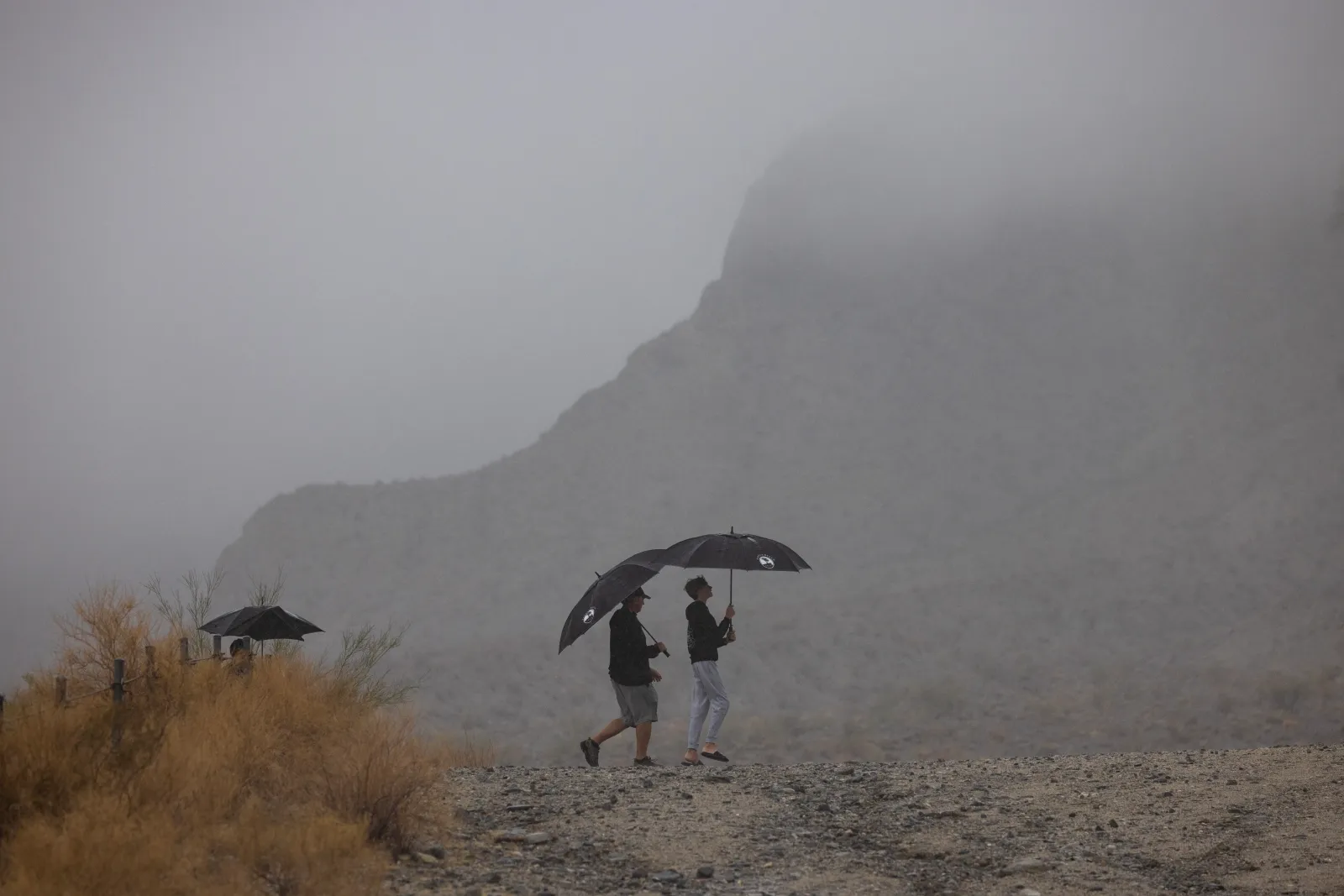 People walk on a desert hiking trail in the rain from Tropical Storm Hilary on August 20, 2023, near La Quinta, California.