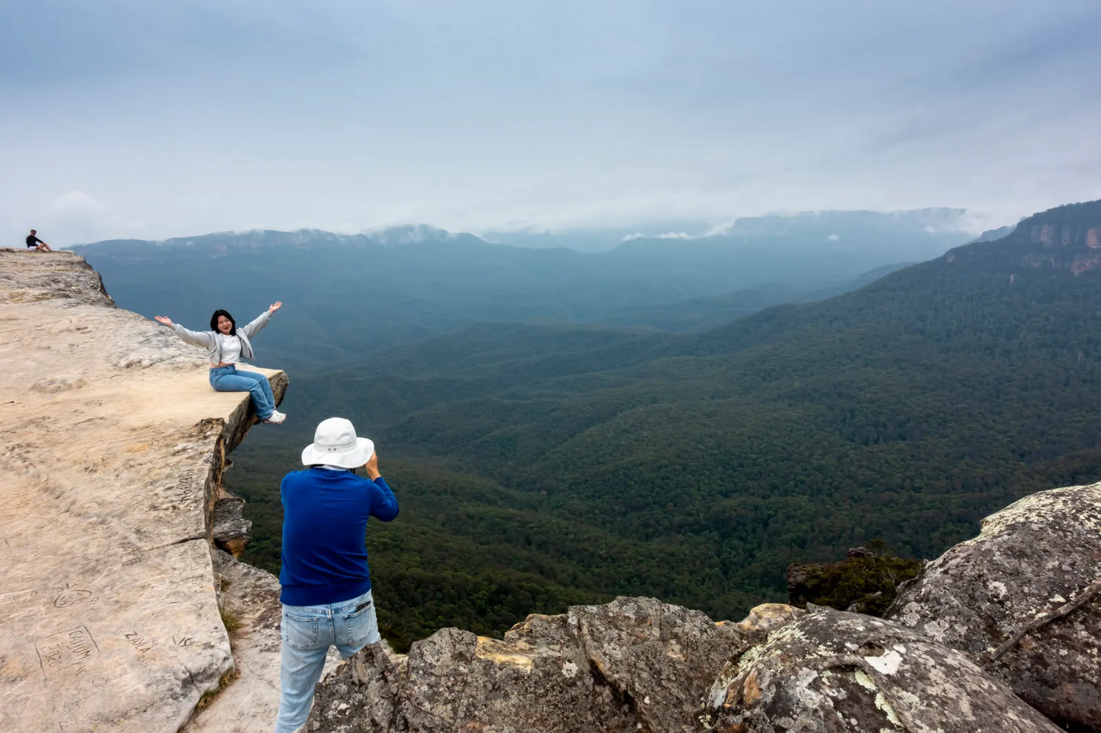 A woman posing for a picture while sitting at the edge of a cliff at Blue Mountains National Park in Sydney, Australia.