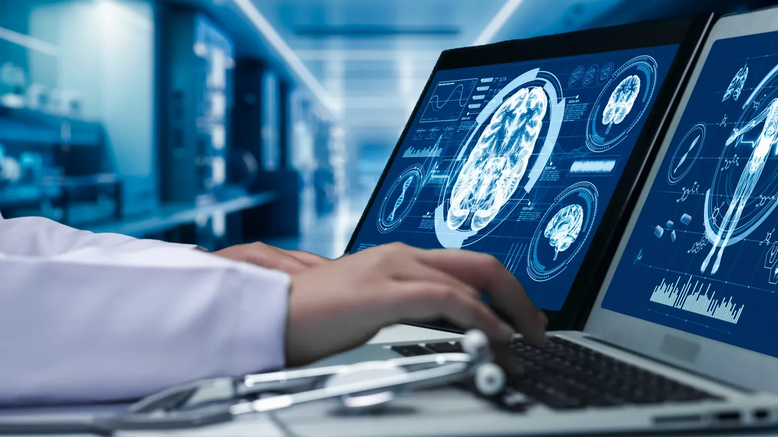 A close up of a doctor working on a laptop with human brain anatomy on display on screen.