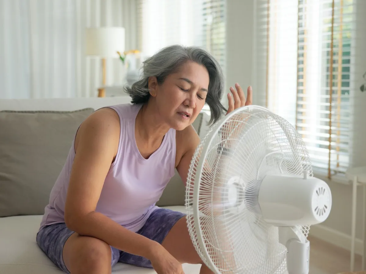 A middle-aged woman sits in front of a fan as she experiences a hot flush.
