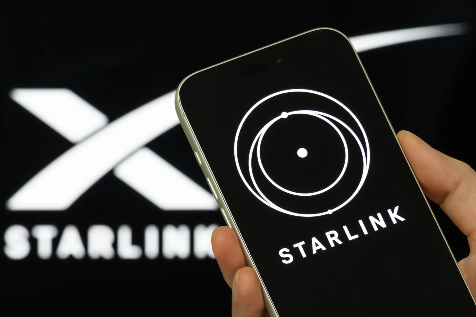 In this photo illustration, a person holds a smartphone displaying the Starlink logo, with SpaceX branding visible in the background, on February 3, 2026, in Chongqing, China.