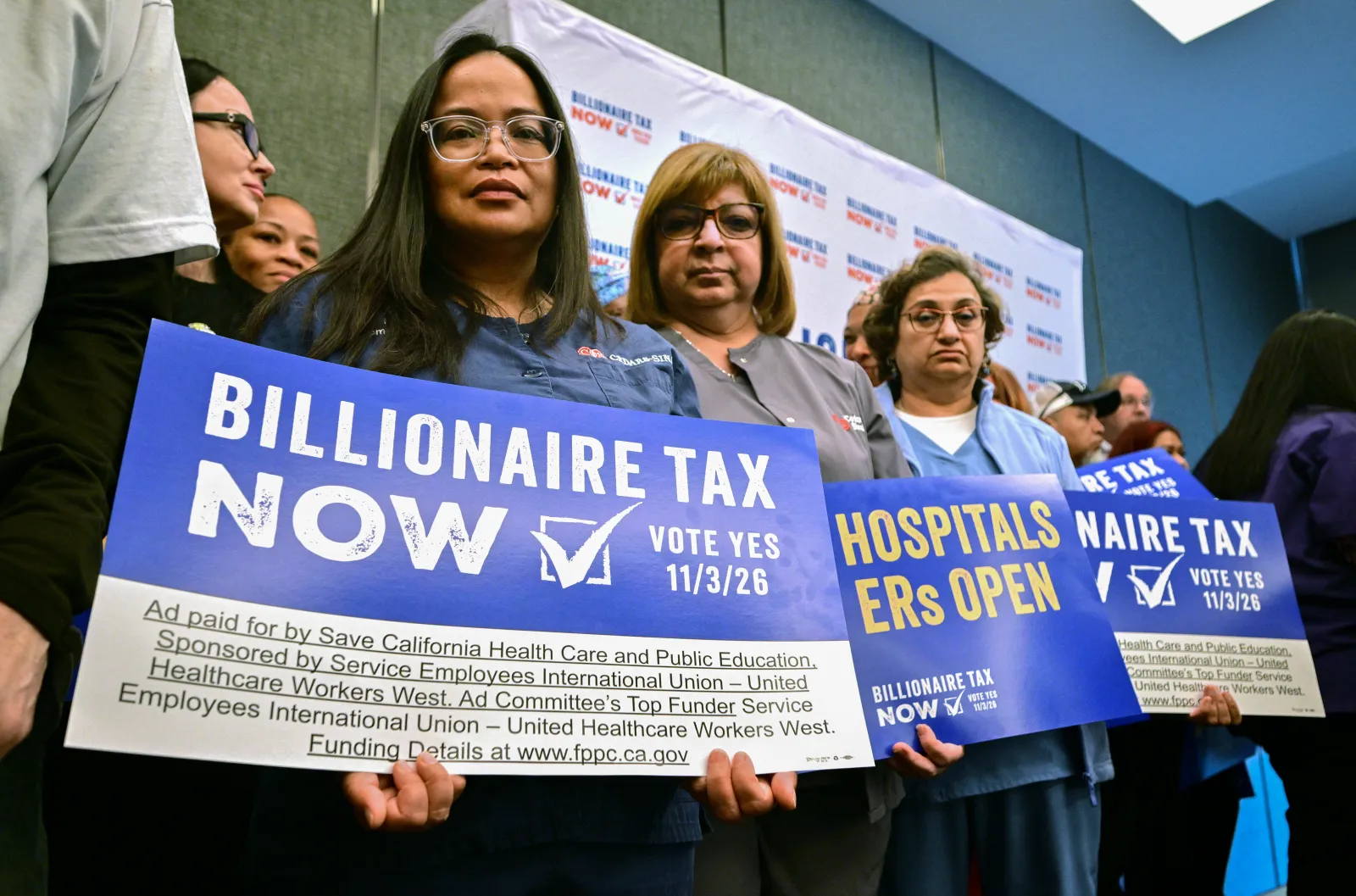 Healthcare workers and other supporters with the Billionaire Tax Now coalition hold signs during a media briefing in Los Angeles on April 27, 2026.