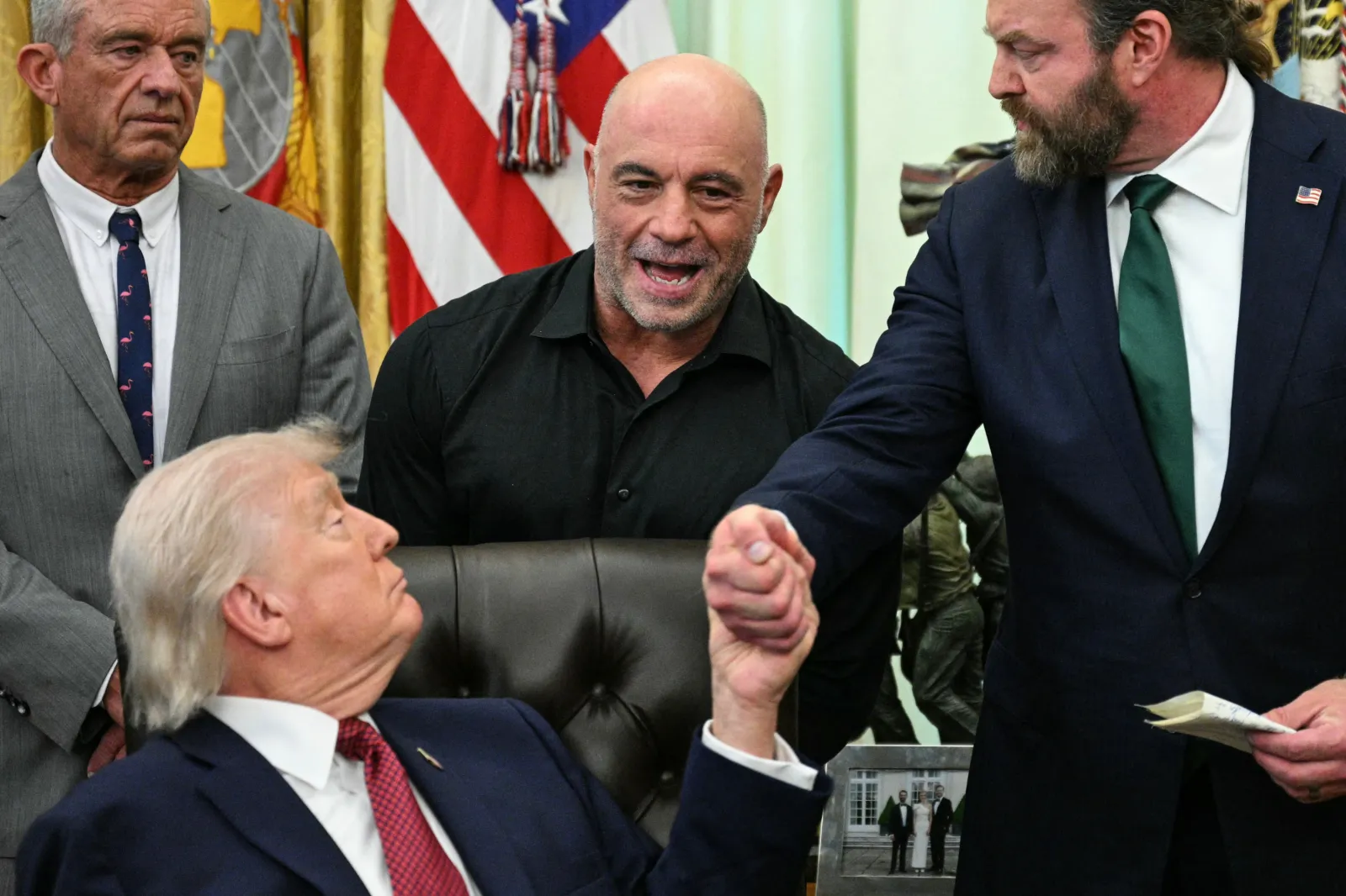 Joe Rogan looks on as U.S. President Donald Trump shakes hands with W. Bryan Hubbard, CEO of Americans for Ibogaine, during an executive order signing ceremony at the White House in Washington, D.C. on April 18, 2026.