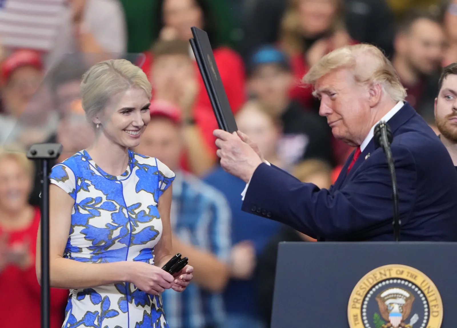 White House aide Natalie Harp hands binders to President Donald Trump before he signs pardons at a campaign rally at the Curtis D. Menard Memorial Sports Center in Wasilla, Alaska, on Tuesday, October 13, 2026,